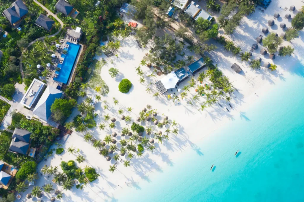 Aerial view of a tropical beach resort with palm trees, villas, and turquoise water in Zanzibar